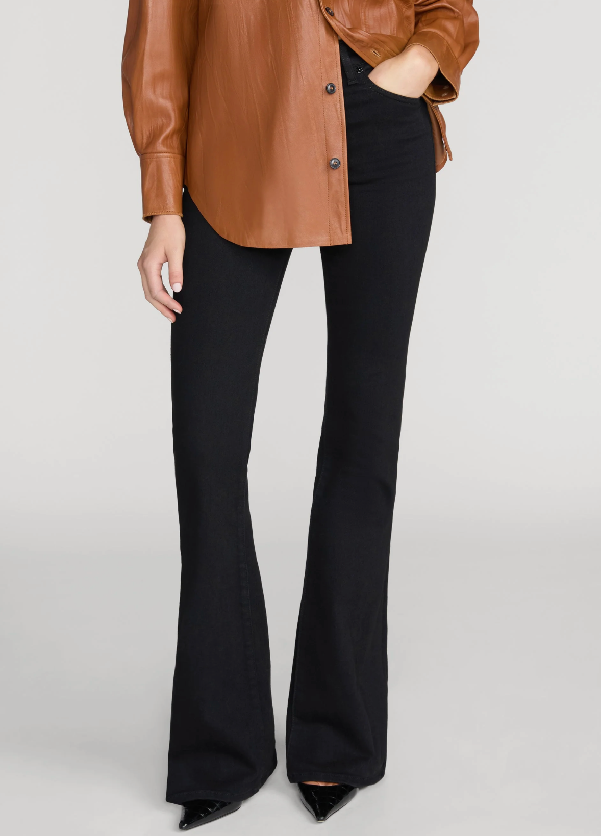 A model wearing black flared pants and a brown leather-look button-up shirt, shown from the waist down against a light gray studio background.