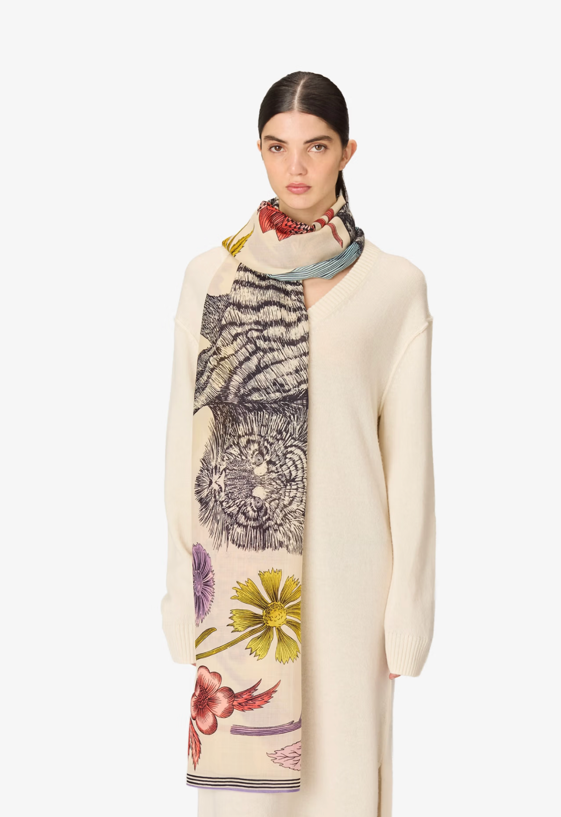A model wearing a cream-colored coat and trousers, styled with a mustard yellow silk scarf featuring a tiger and floral print, against a plain white background.
