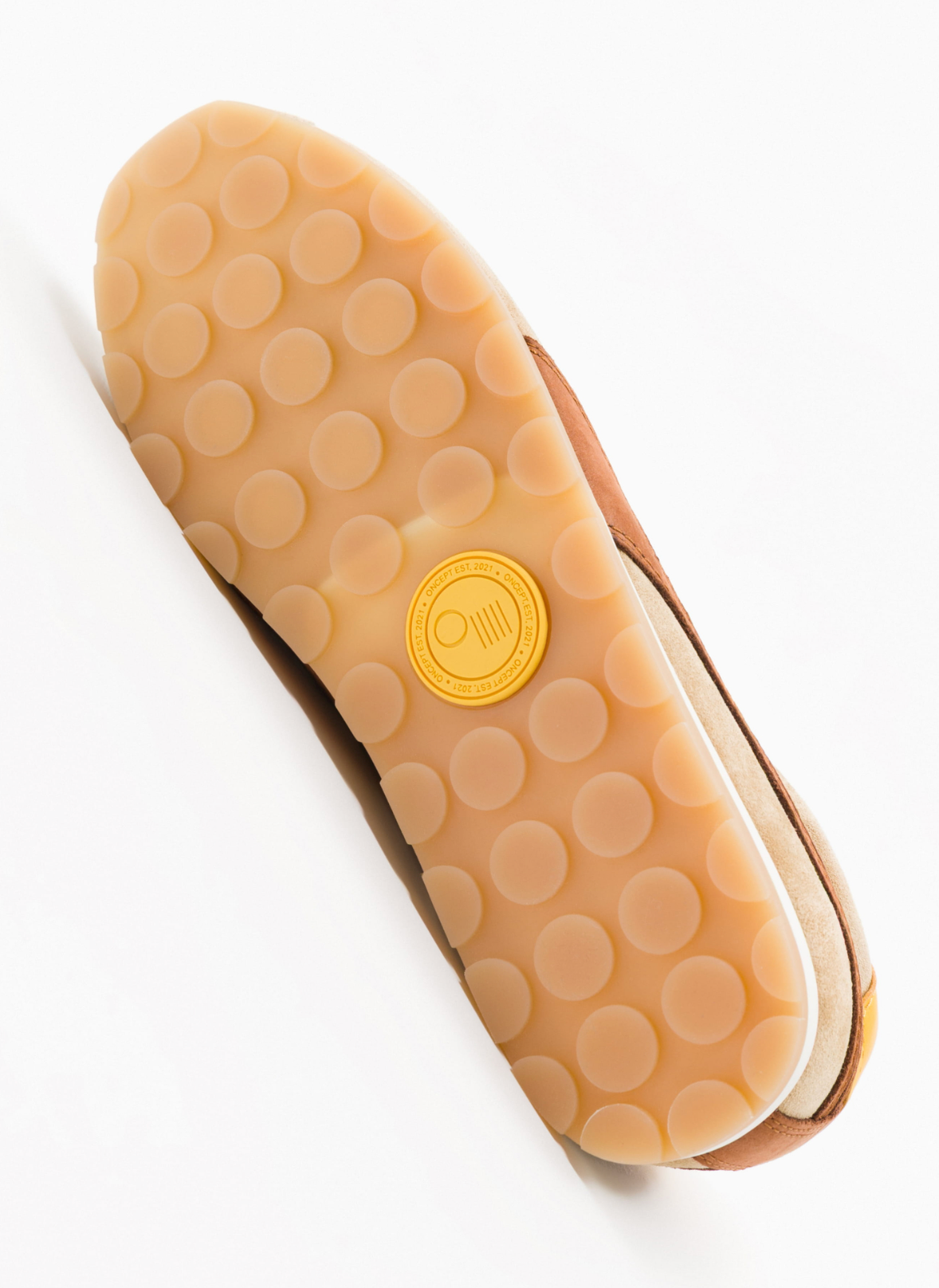 Top-down view of a shoe sole showing a tan circular bubble tread pattern and a yellow circular logo stamp in the center, photographed on a clean white background.