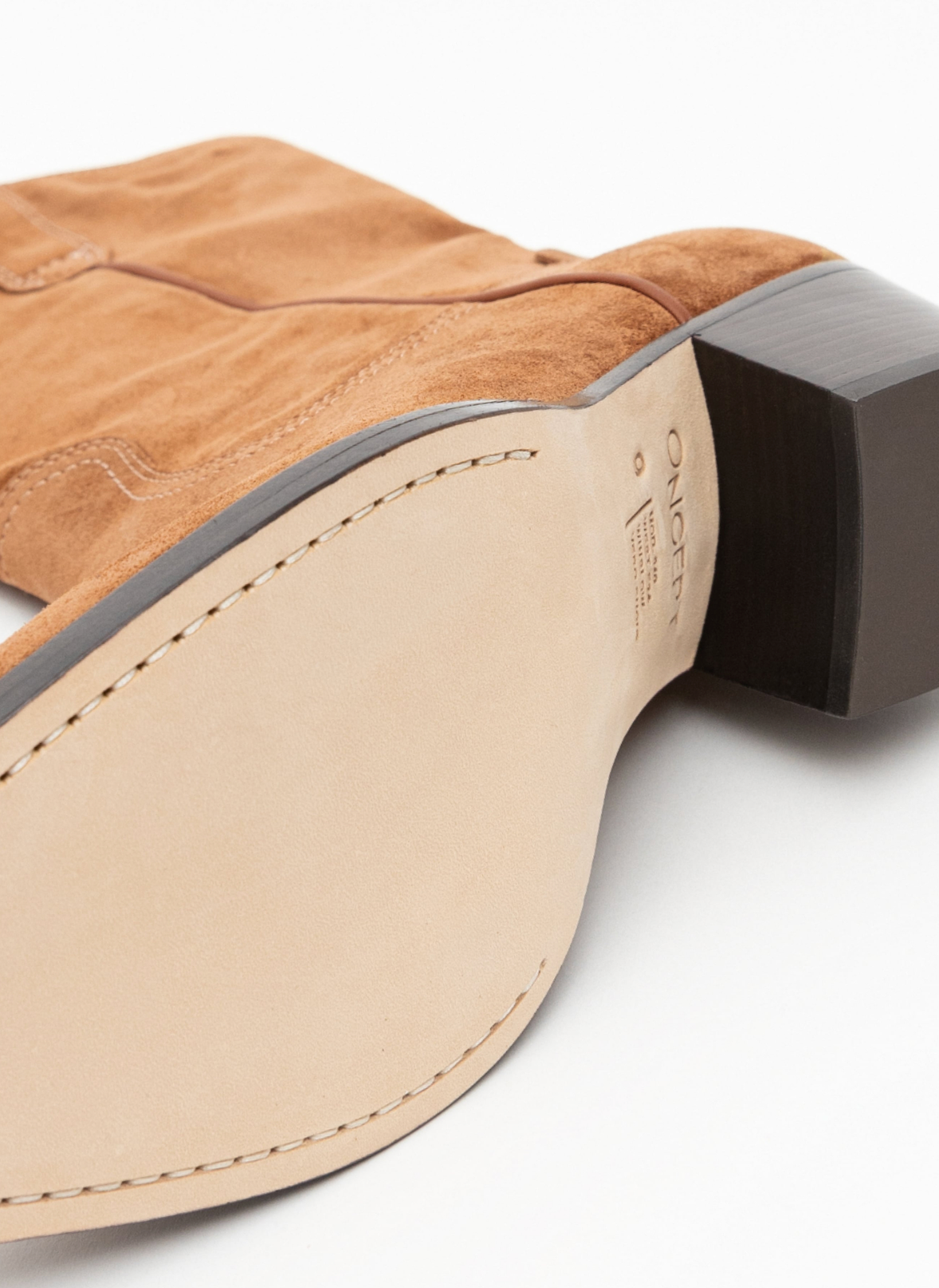 Close-up of the heel and sole of a tan suede boot with a beige leather insole and a dark brown block heel on a white background.