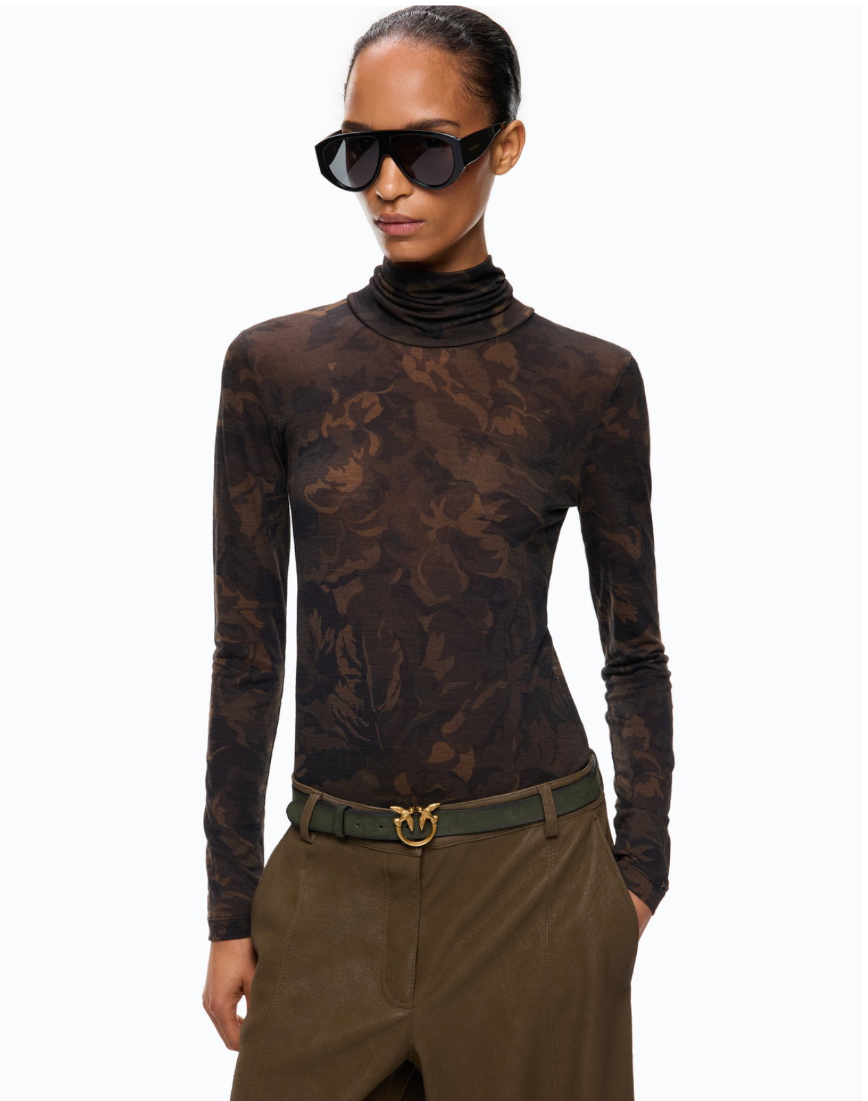 A model wearing a sheer, long-sleeve cowl-neck top with a dark brown floral jacquard pattern, styled with olive green trousers and a belt, against a plain white background.