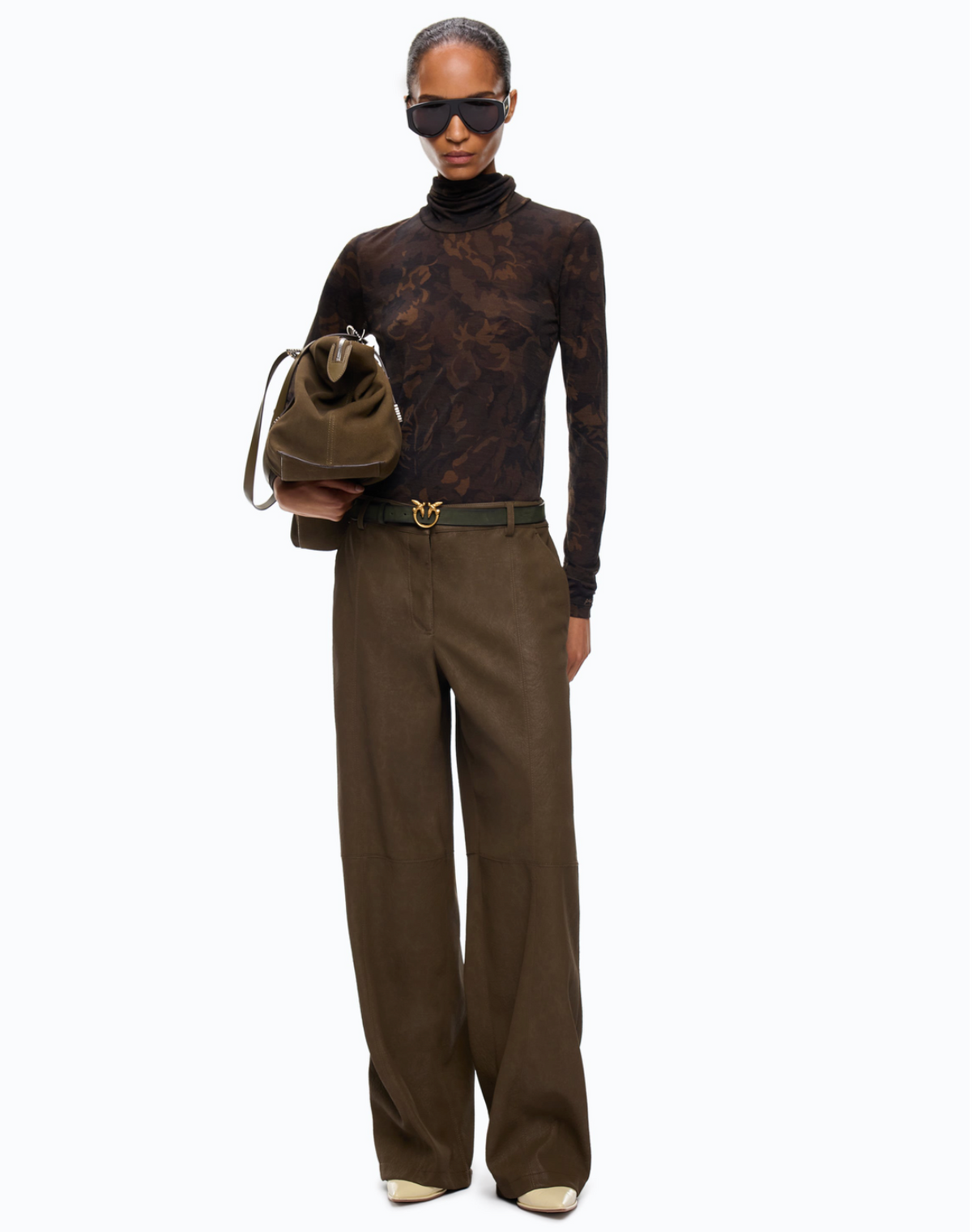 A model wearing a sheer, long-sleeve cowl-neck top with a dark brown floral jacquard pattern, styled with olive green trousers and a belt, against a plain white background.