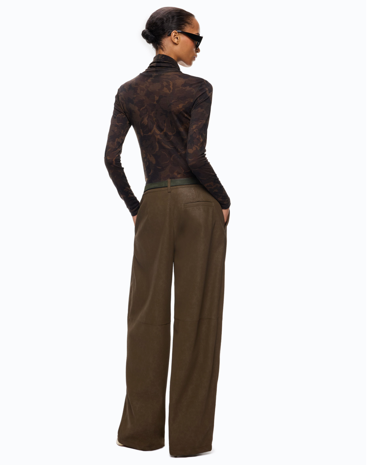 A model shown from the back wearing a dark brown patterned long-sleeve turtleneck top and wide-leg brown trousers, styled with black sunglasses against a plain white background.