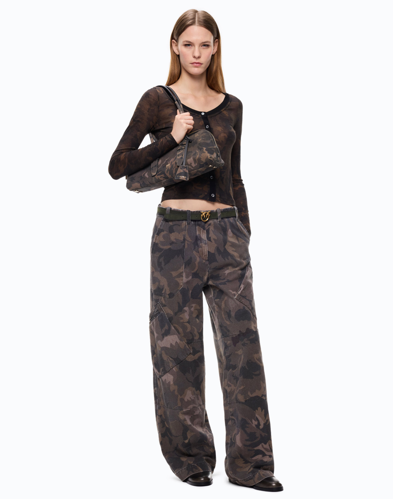 A person wearing wide-leg camouflage pants with a dark olive belt and black shoes, shown from the waist down against a plain white studio background.