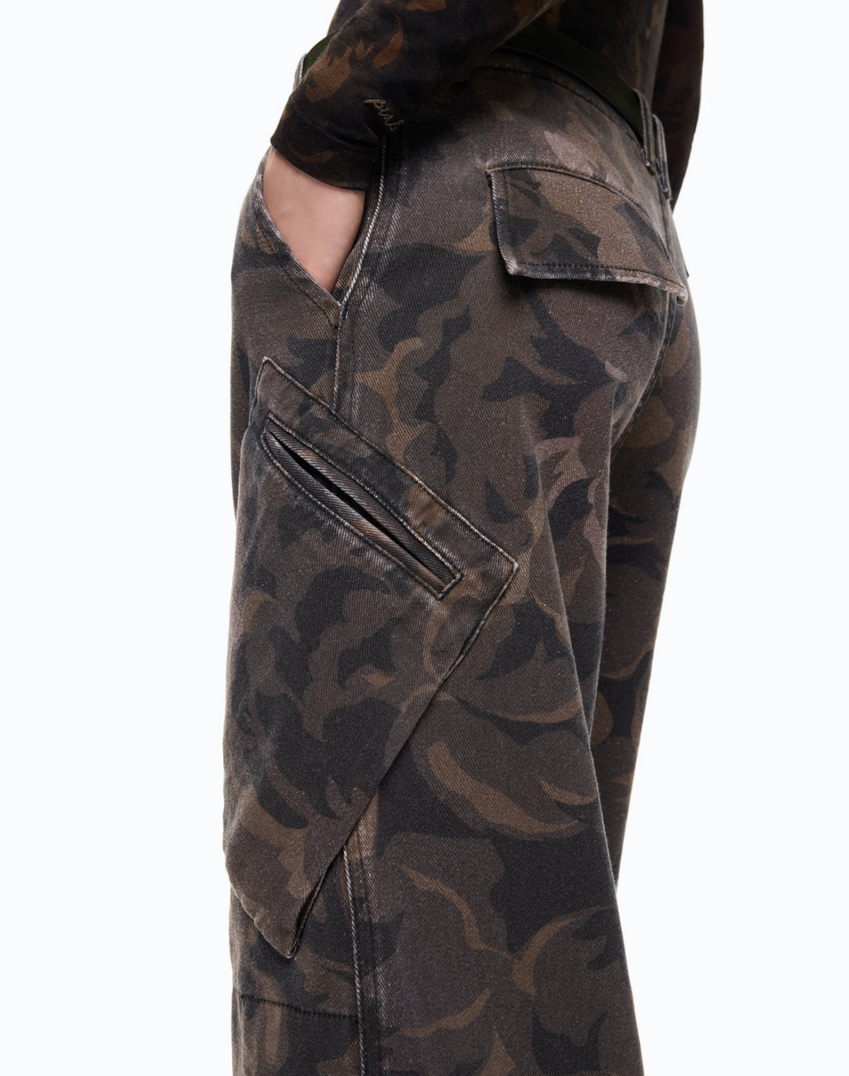 Close-up side view of a person wearing dark camouflage cargo pants with a hand in a pocket, against a plain white background.