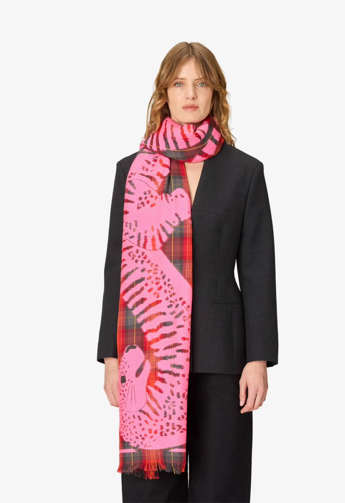 A model wearing a black blazer and black trousers, styled with a vibrant pink and red patterned scarf featuring a leopard print and tartan plaid.