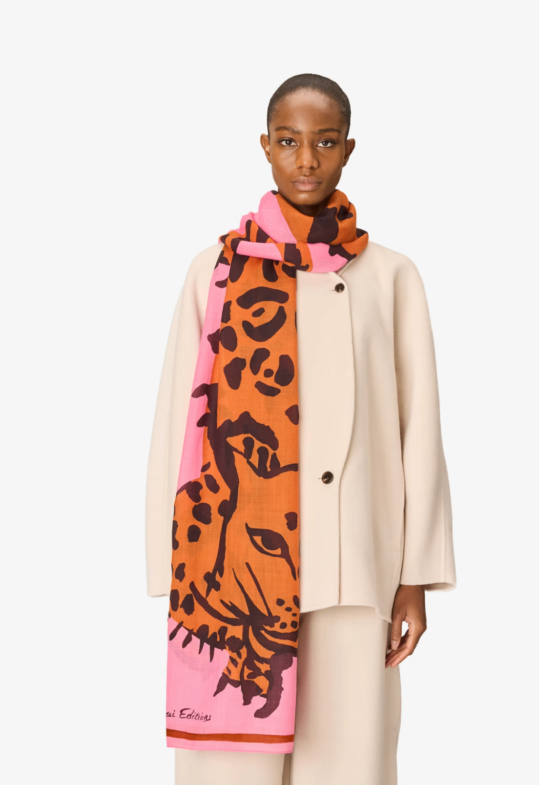 A model wearing a beige coat and trousers, styled with a vibrant scarf featuring a pink and orange leopard print design with a tiger face motif. The brand name 'Missoni' is visible in script on the bottom left corner of the scarf.