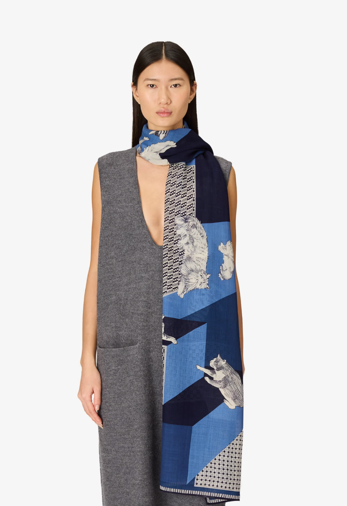 A model wearing a gray sleeveless dress and a blue patterned scarf with illustrations of cats, photographed against a plain light gray background.