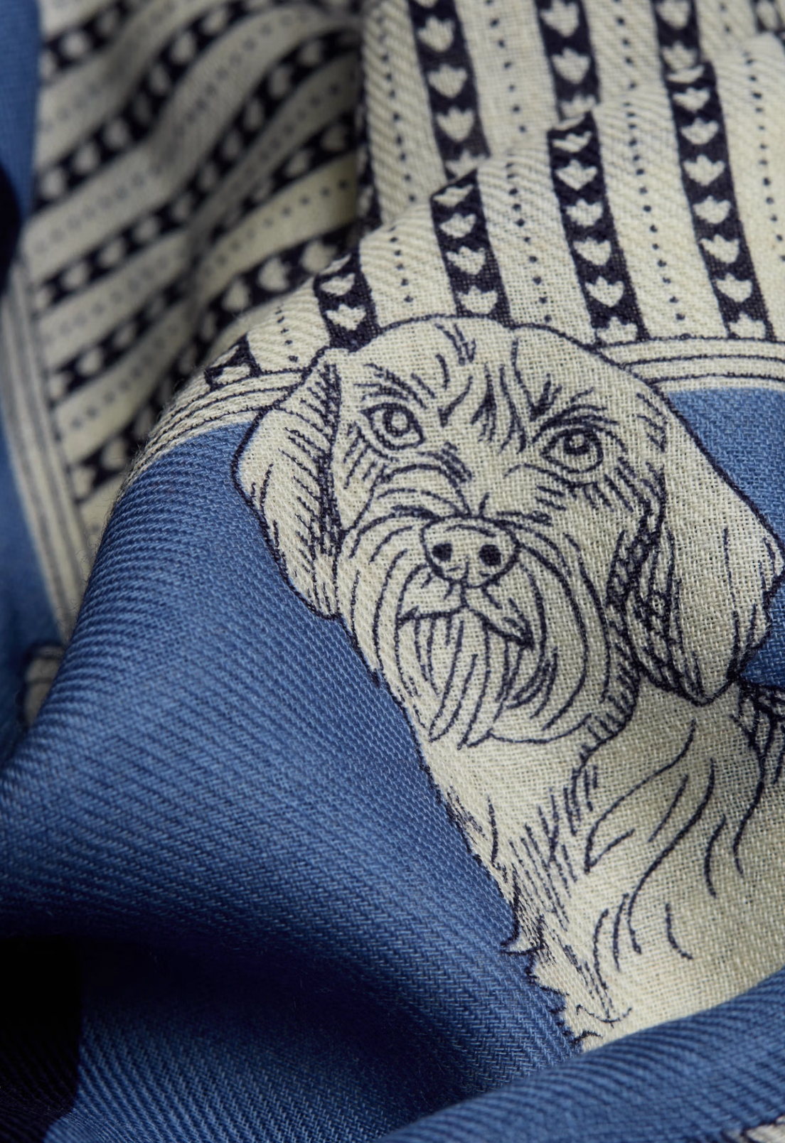 A close-up of a blue patterned fabric featuring a detailed black line art illustration of a dog's face, with geometric and striped patterns in the background.