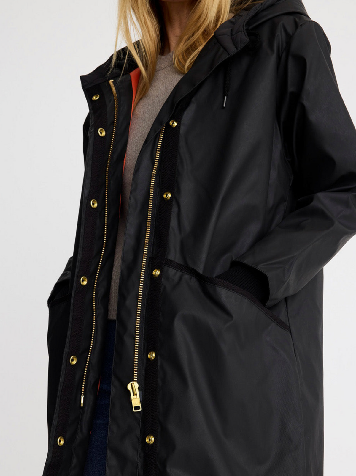 A close-up of a person wearing a black hooded jacket with prominent gold-tone metal zippers and snap buttons, layered over a gray top.