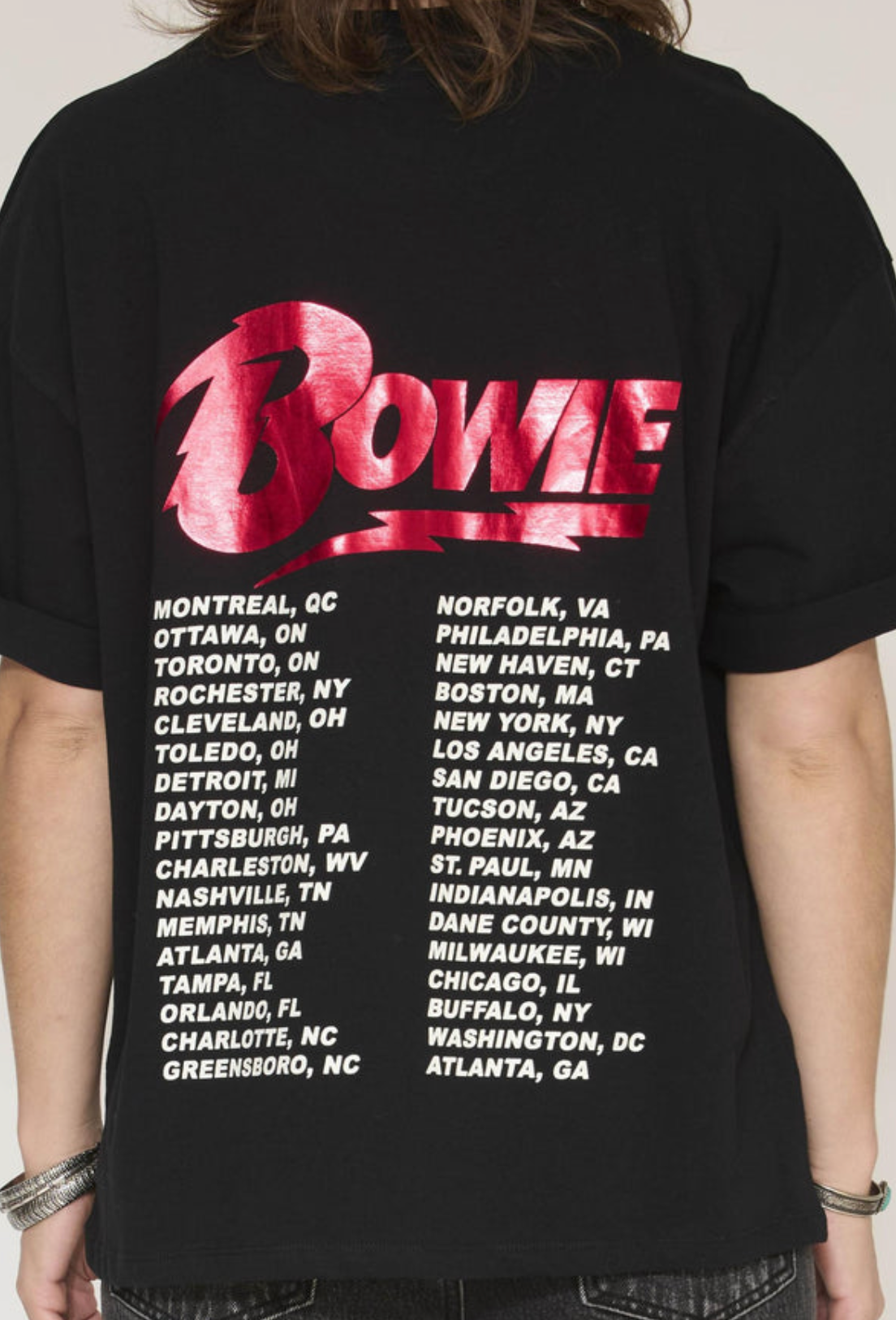 A person wearing a black t-shirt with a large red and white 'Bowie' graphic and a list of tour cities printed on the back.