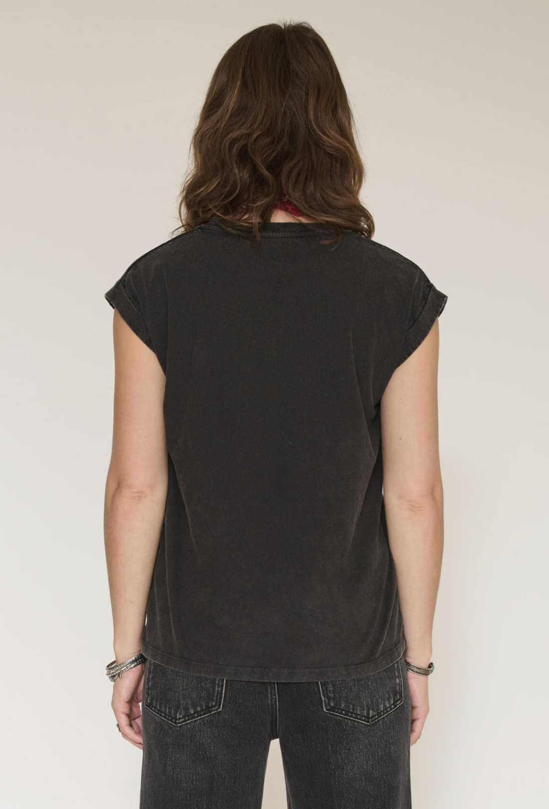A woman viewed from the back wearing a washed black short-sleeve t-shirt and dark gray jeans against a plain off-white background.