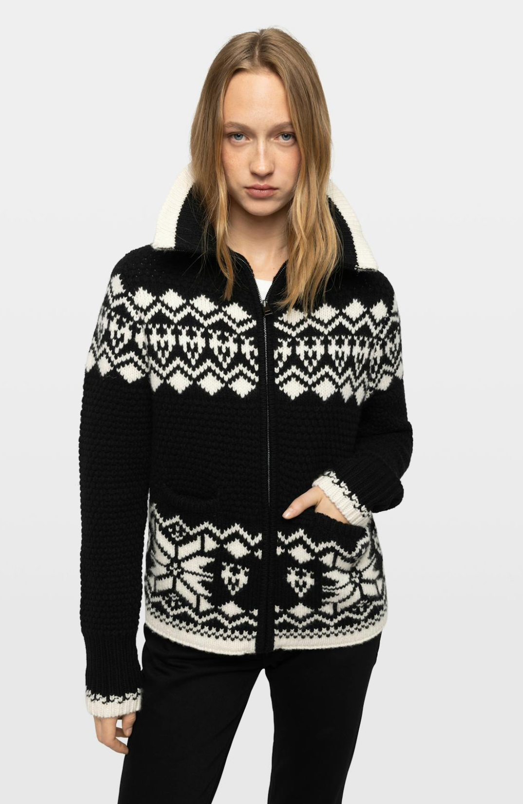 A woman modeling a black and white knit zip-up cardigan with a white sherpa-lined hood, photographed against a light gray studio background.