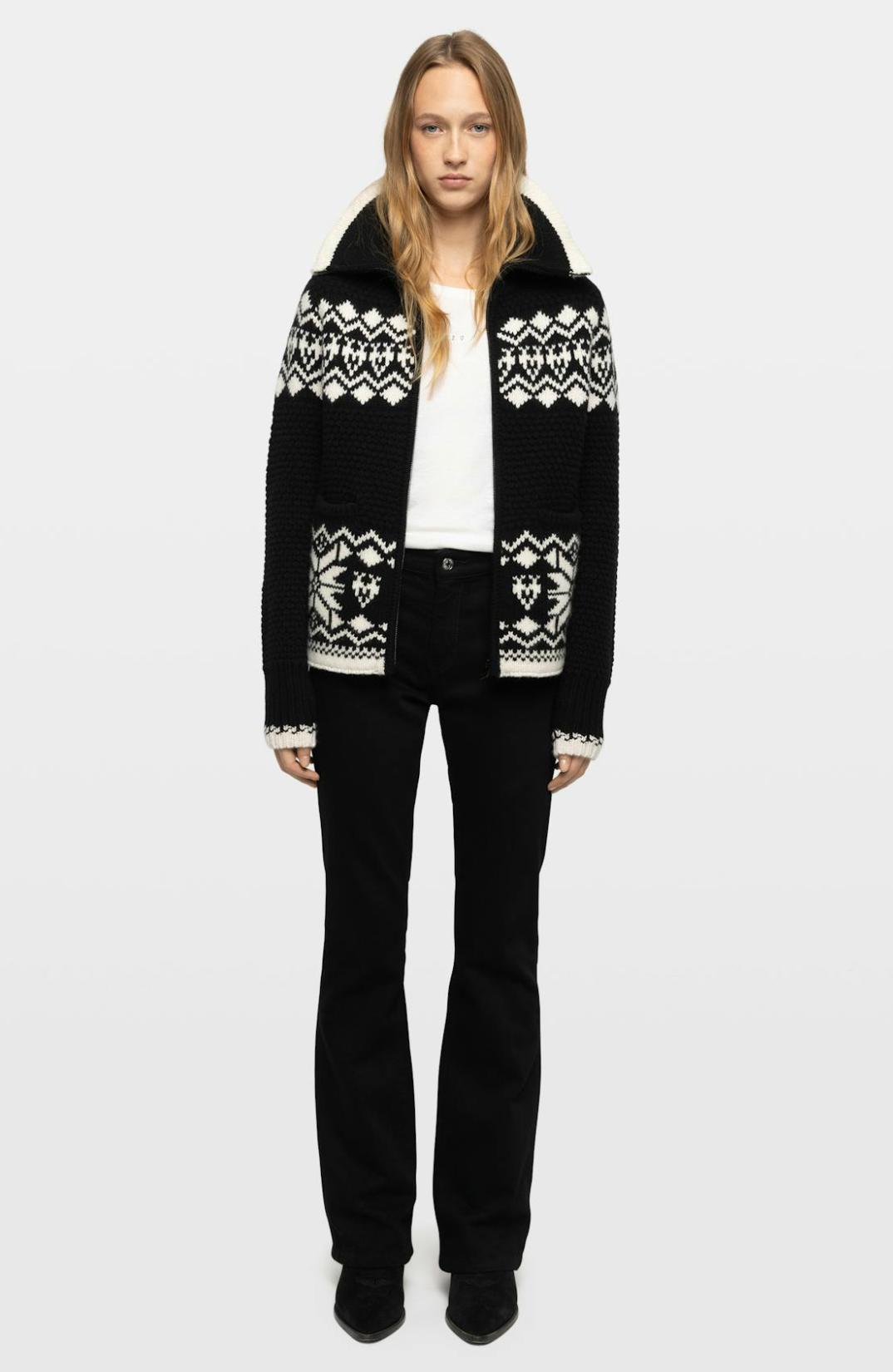 A woman modeling a black and white knit zip-up cardigan with a white sherpa-lined hood, photographed against a light gray studio background.